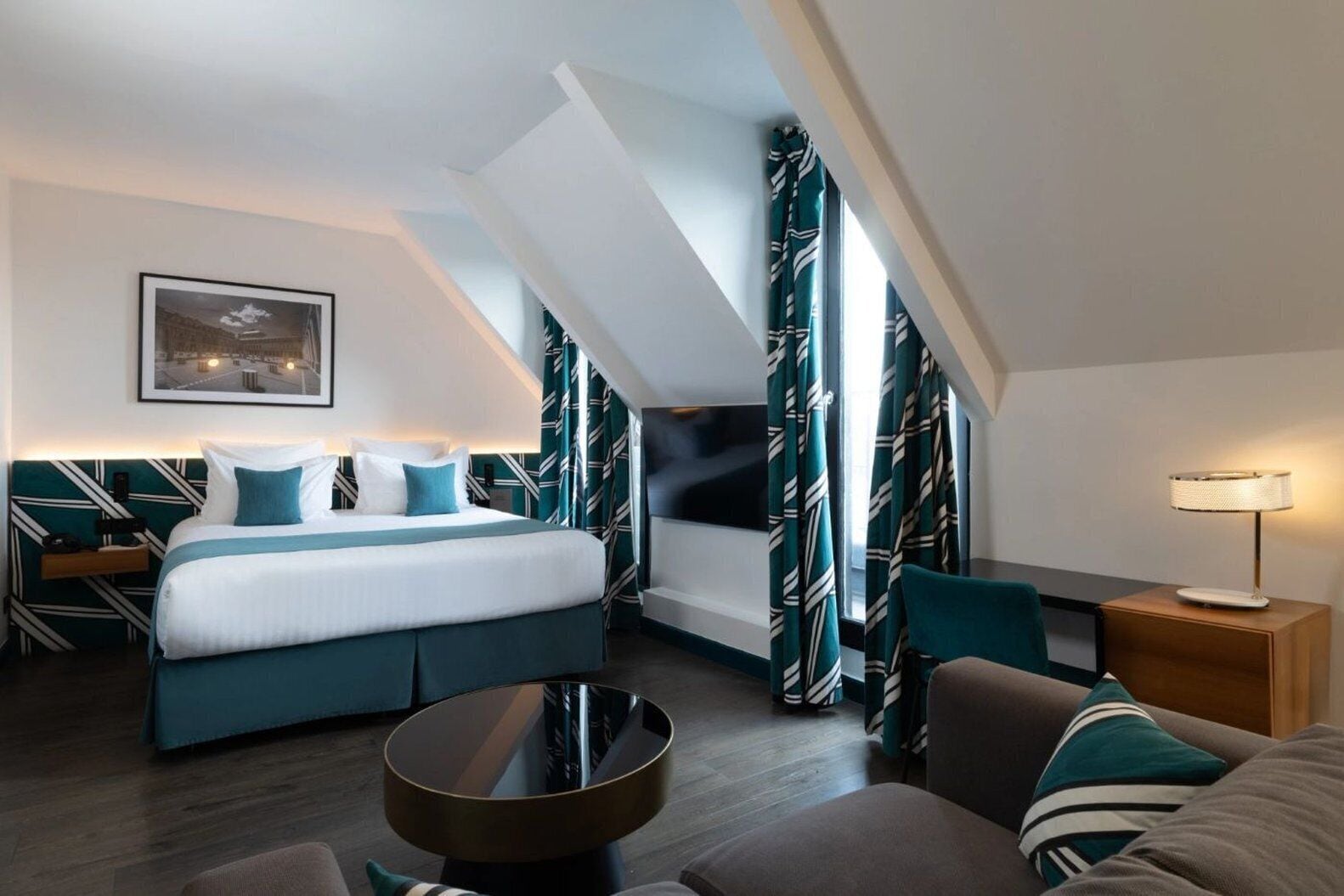 Una habitación de hotel moderna con una cama grande, un escritorio, una silla, una mesa de centro redonda y una lámpara.