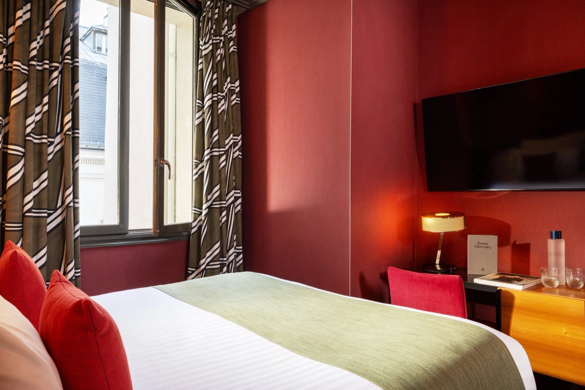 A hotel room with a bed, a desk, a chair, a TV, and a lamp.