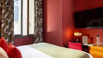 A hotel room with a bed, a desk, a chair, a TV, and a lamp.