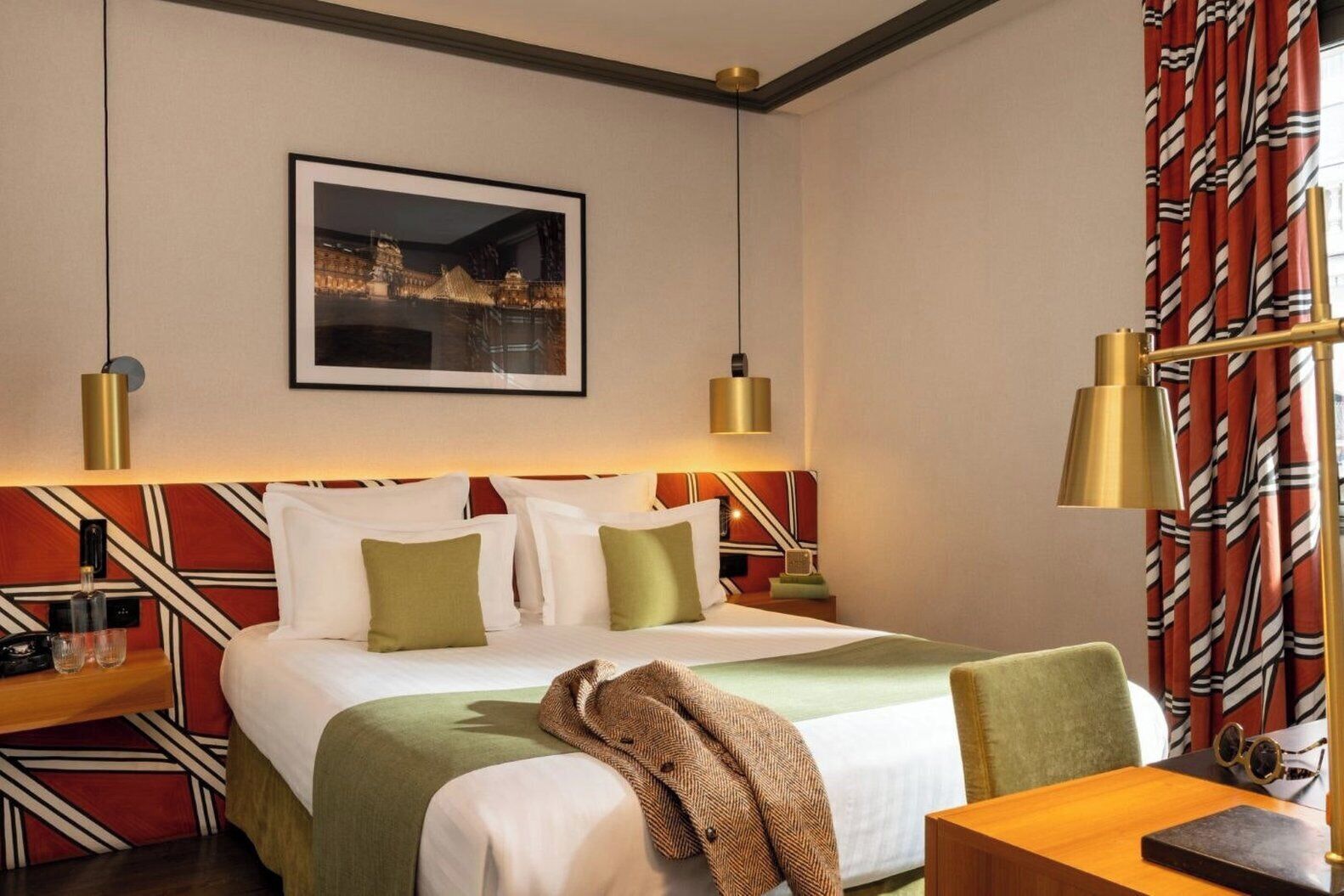 Een hotelkamer met een bed, nachtkastjes, een bureau, een stoel, een lamp en een ingelijst kunstwerk aan de muur.