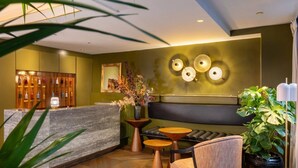 A modern reception area with a marble reception desk, a black upholstered sofa, and a wooden coffee table. - Hôtel Aoriste & Spa (Paris)