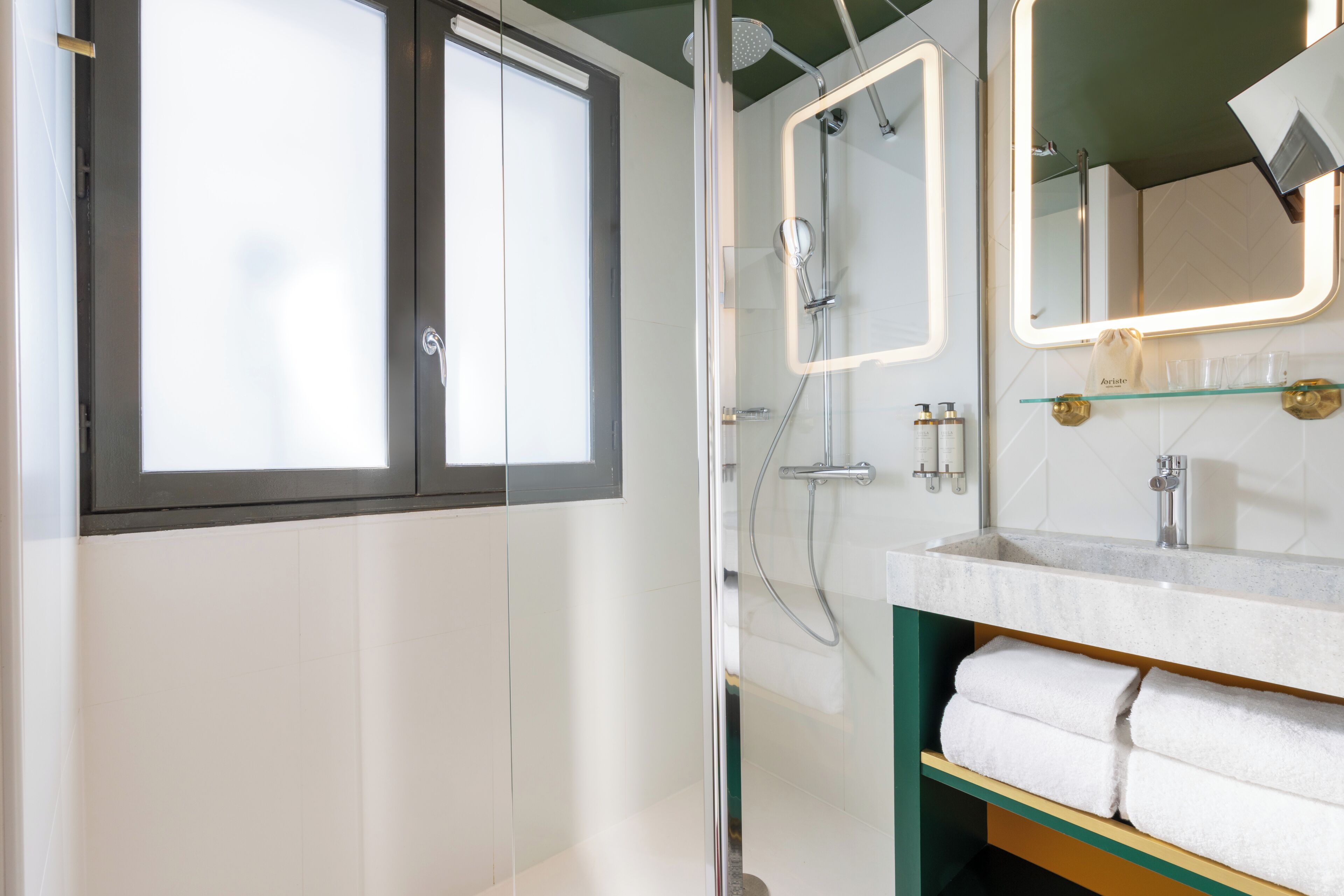 A modern bathroom with a glass-enclosed shower, a vanity with a mirror, and a shelf with towels.