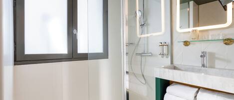 A modern bathroom with a glass-enclosed shower, a vanity with a mirror, and a shelf with towels.