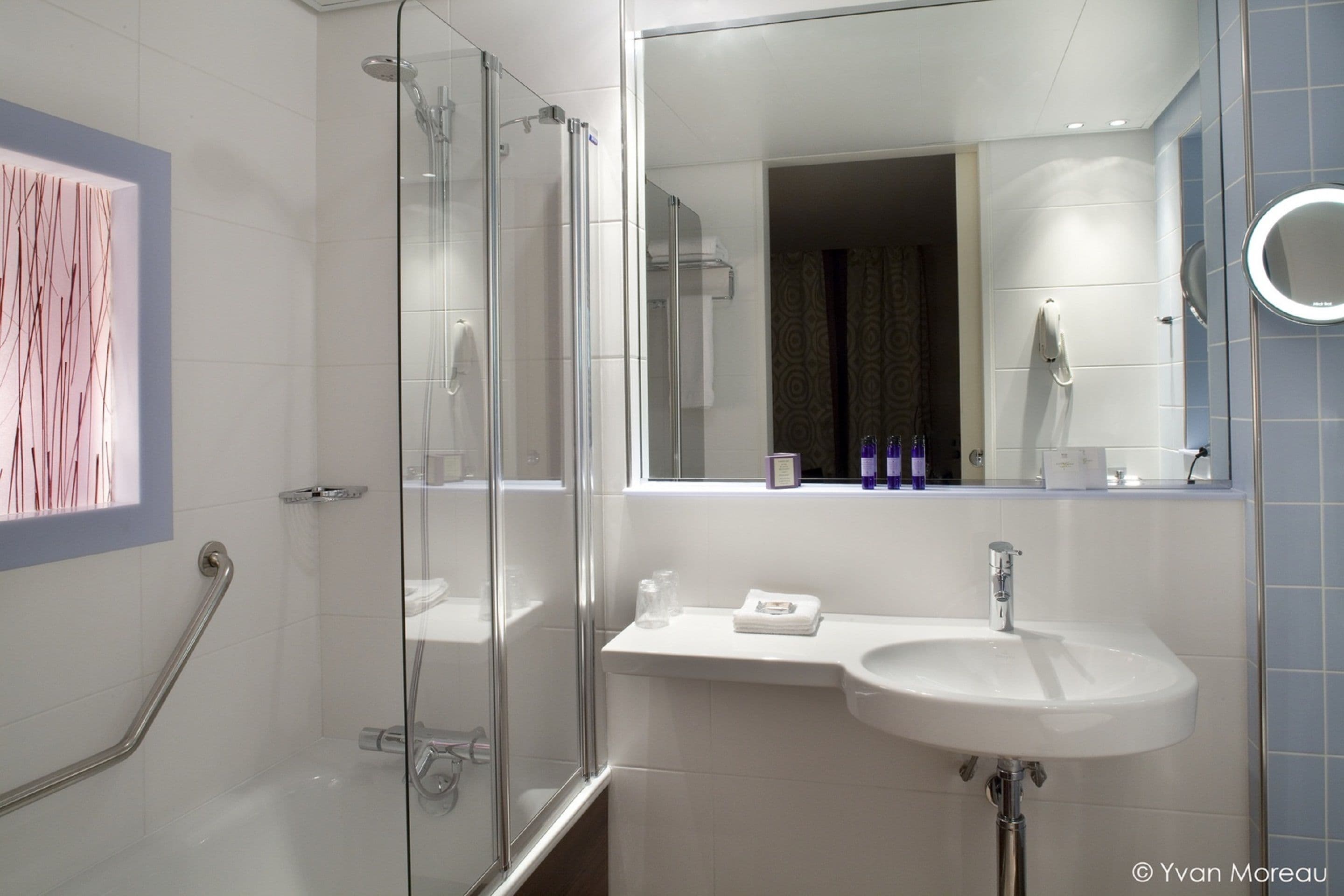 Une salle de bain moderne avec une douche à l’italienne en verre, un lavabo blanc et un grand miroir.