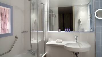 Une salle de bain moderne avec une douche à l’italienne en verre, un lavabo blanc et un grand miroir.