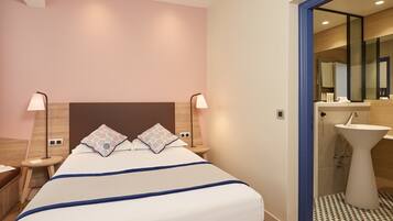 A hotel room with a bed, bedside lamps, a nightstand, a bathroom with a sink and mirror.