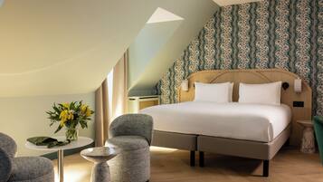Une chambre d’hôtel avec un grand lit, une table ronde, une chaise et un vase de fleurs.