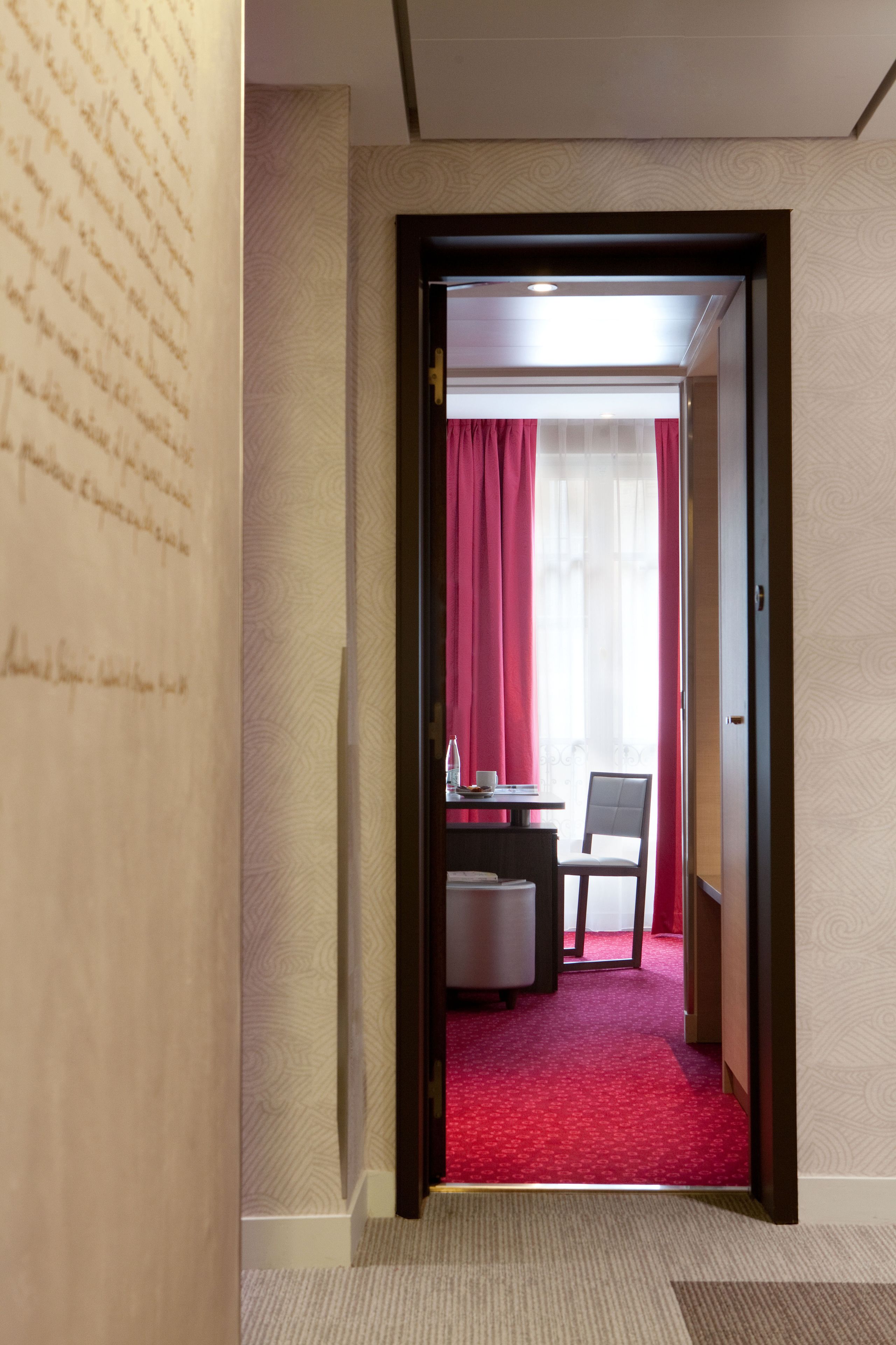Ein Hotelzimmer mit rotem Teppich, einem Schreibtisch mit Stuhl und einem Fenster mit roten Vorhängen.