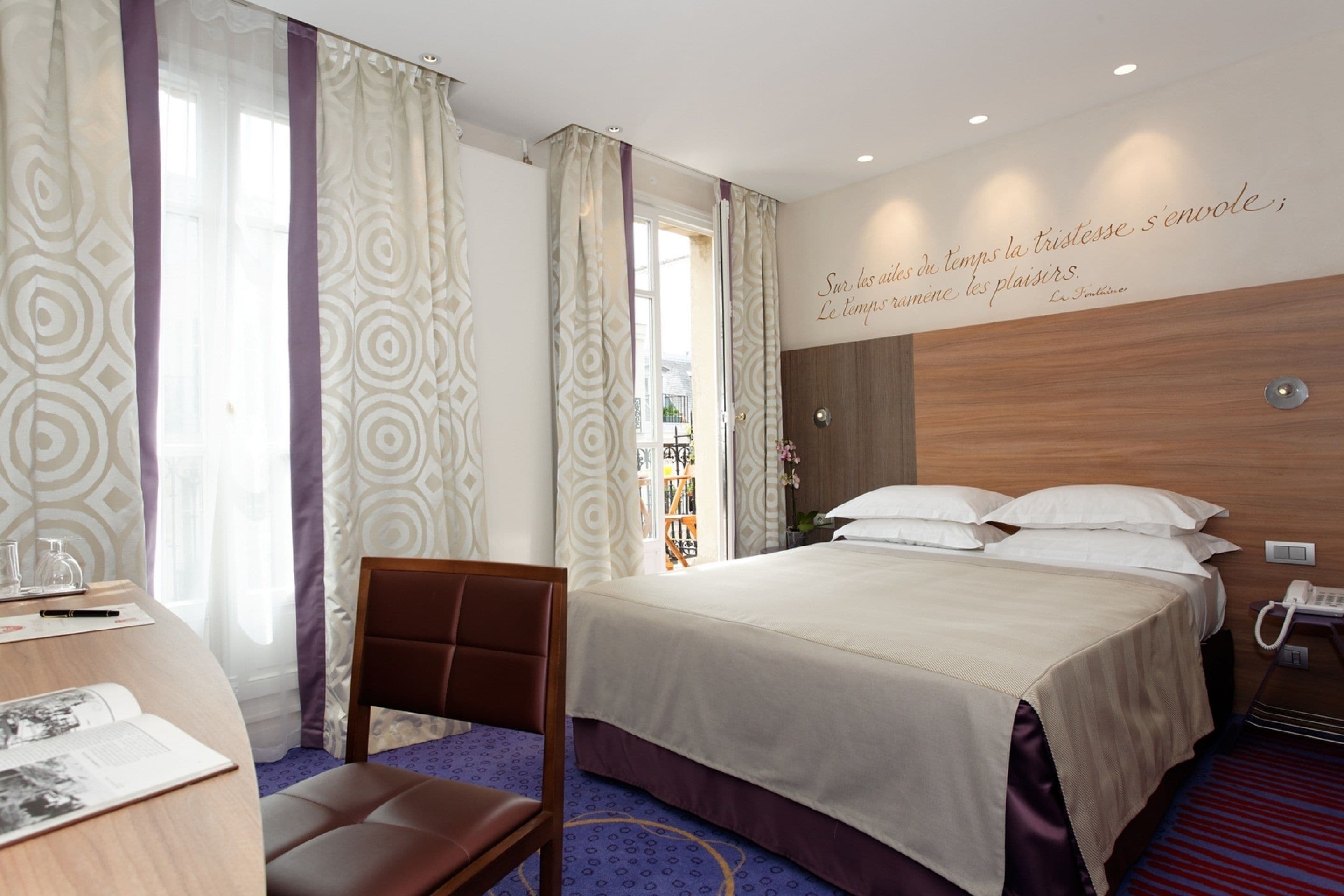 Una habitación de hotel con cama, escritorio con silla, teléfono y una pared con una cita.