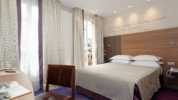 Una habitación de hotel con cama, escritorio con silla, teléfono y una pared con una cita.