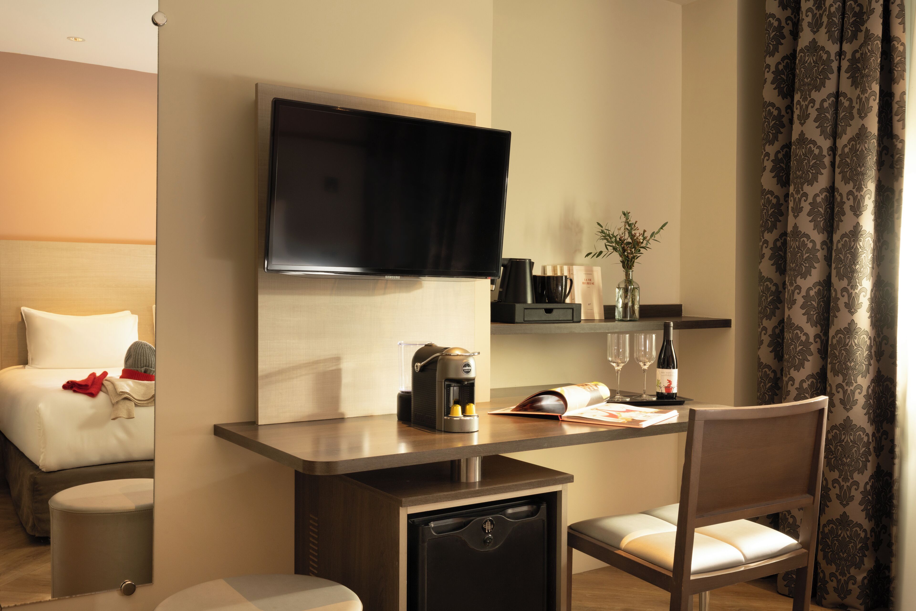 Una habitación de hotel con una cama, un escritorio con cafetera, un televisor y una silla.