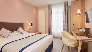 Habitación de hotel con cama, escritorio con ordenador portátil, silla, televisión y ventana con cortinas.