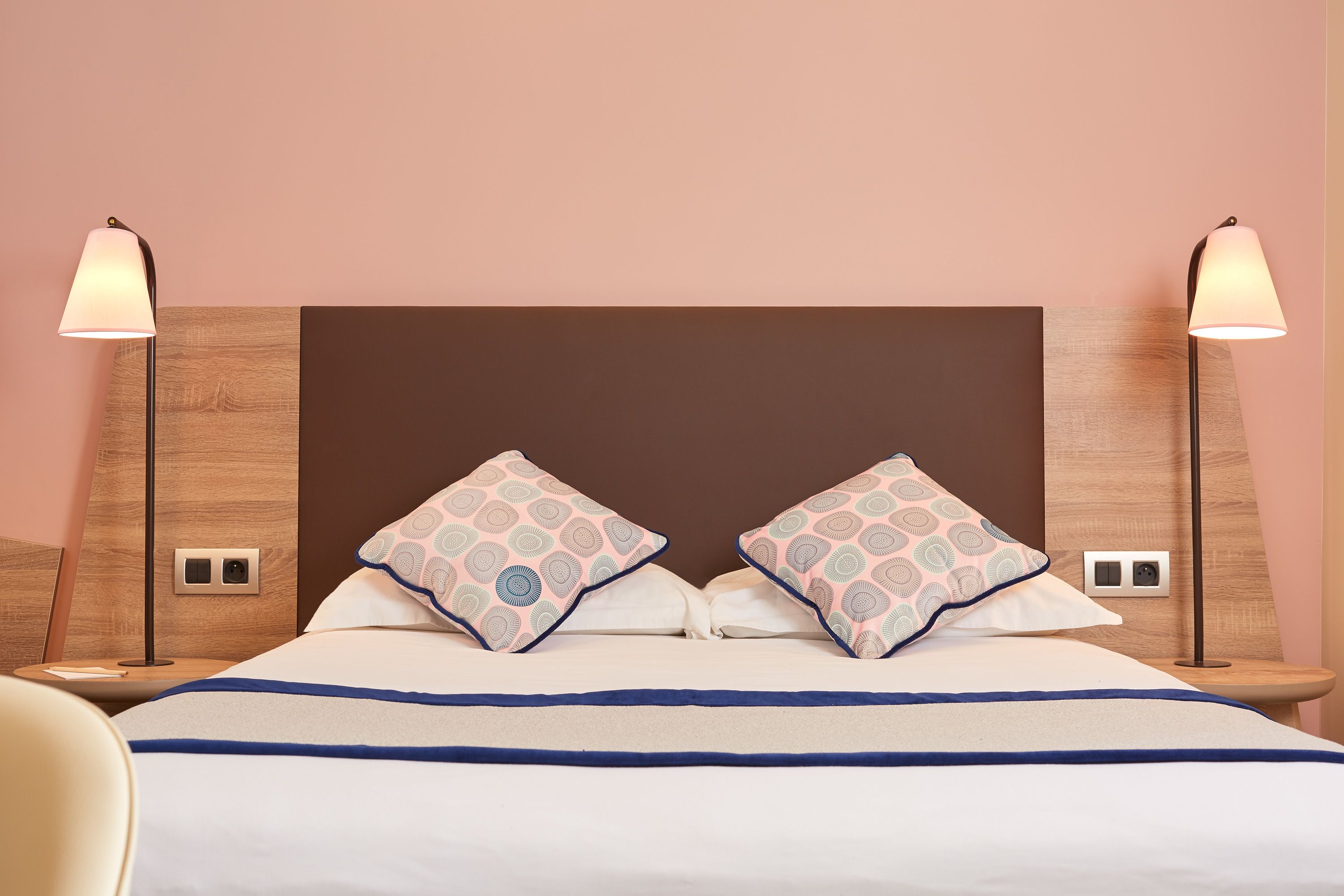 A neatly made bed with patterned pillows, a wooden headboard, bedside lamps, and a nightstand with a lamp.