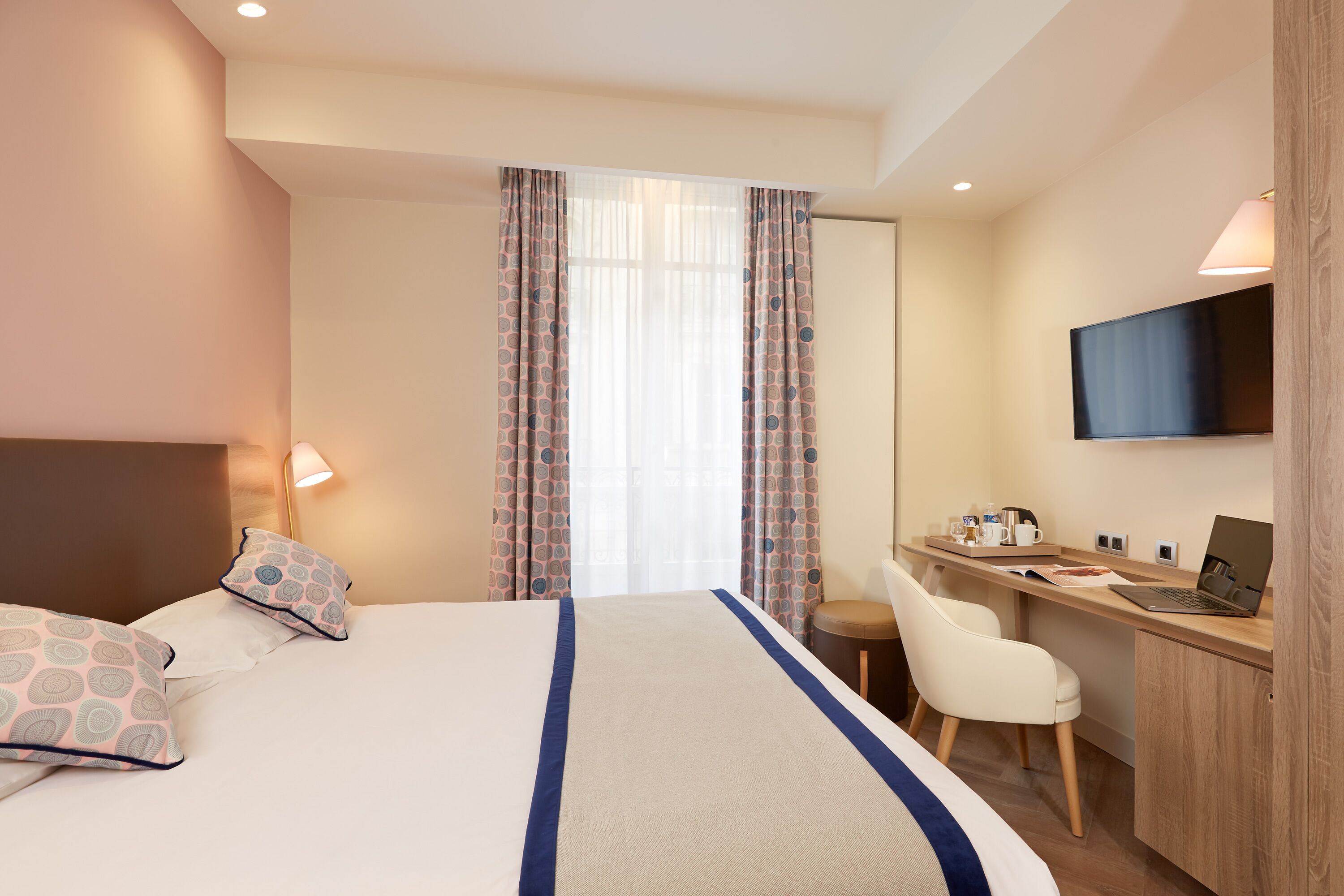 A hotel room with a bed, a desk, a chair, a TV, and curtains.