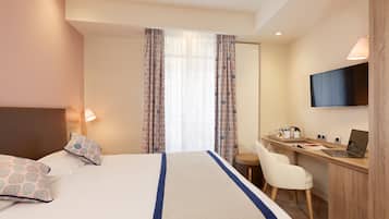 A hotel room with a bed, a desk, a chair, a TV, and curtains.