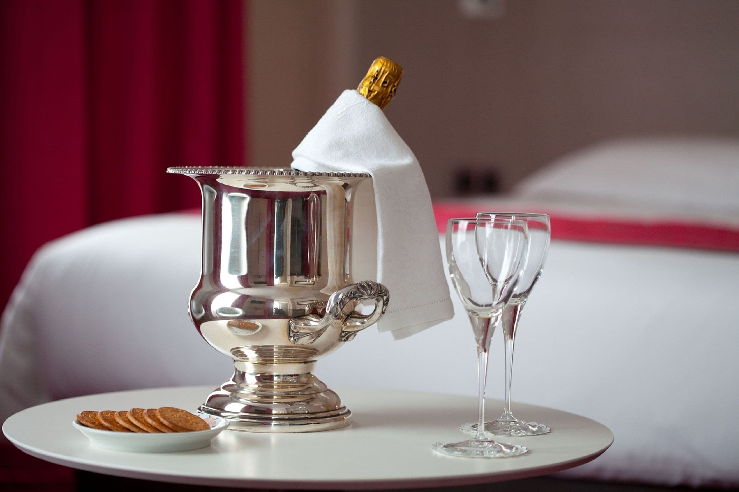 Une théière en argent surmontée d’un couvercle doré, une serviette blanche et deux verres vides sur une table blanche.
