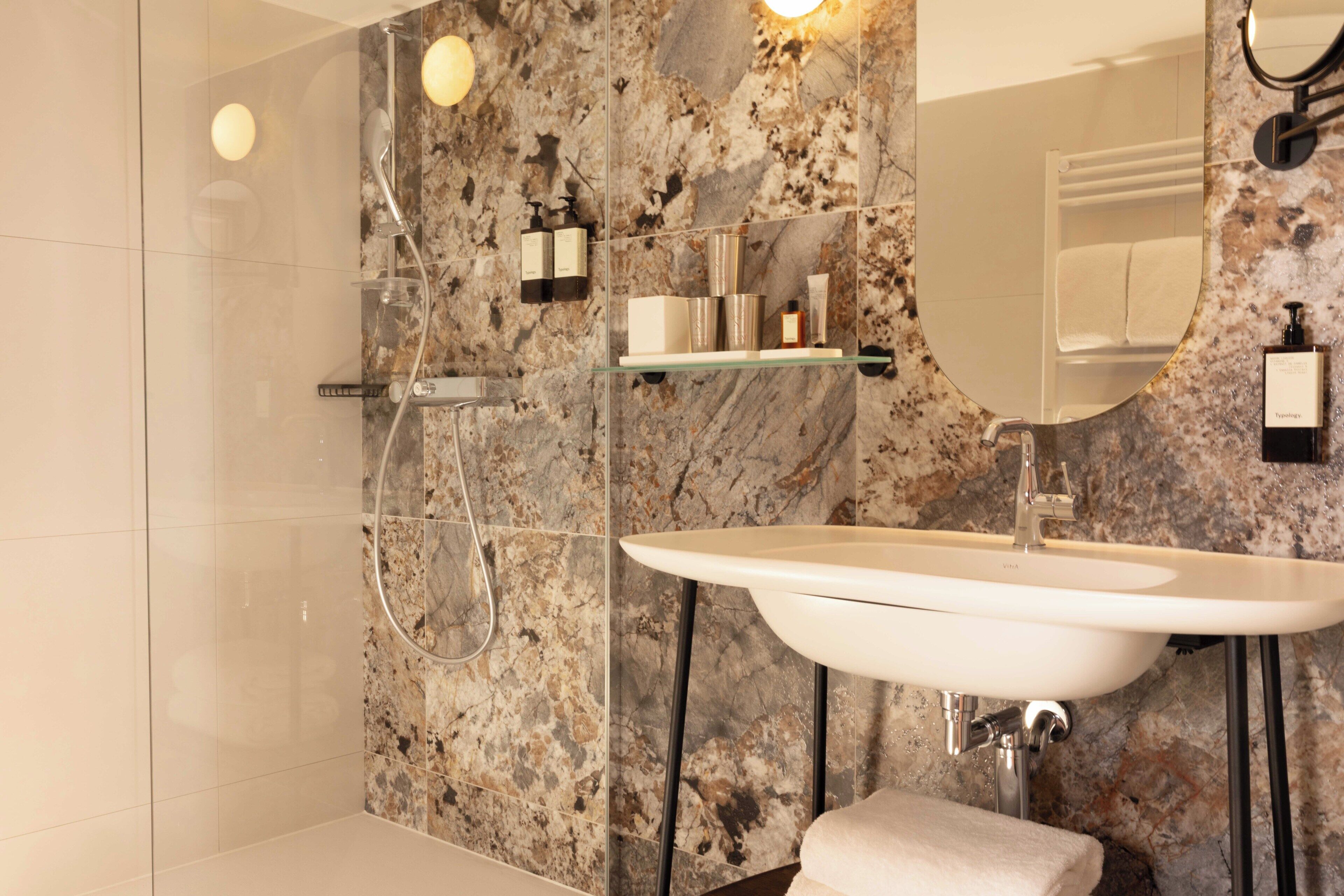 Un baño con pared de mármol, un lavabo, un espejo y una ducha.