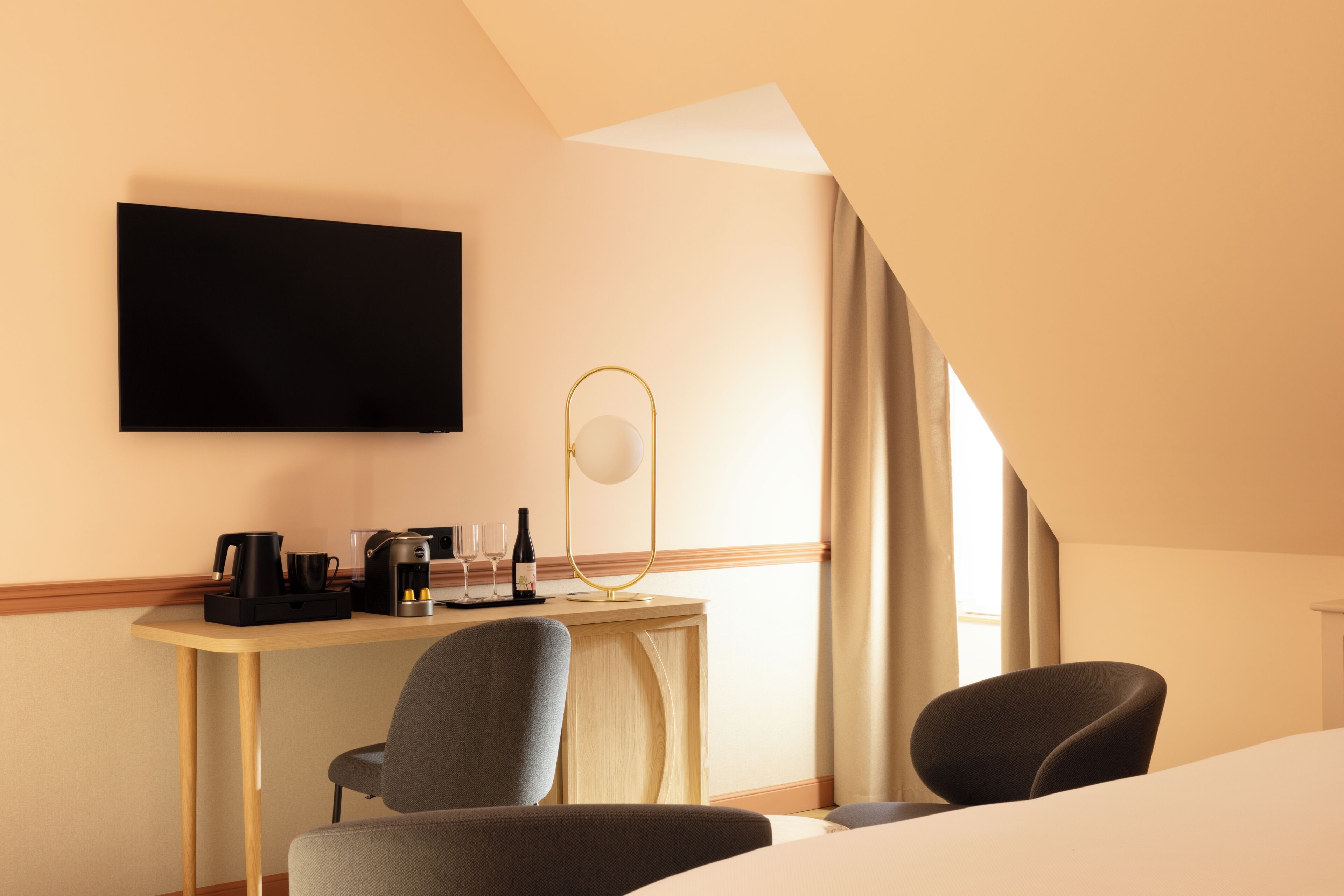 Quarto de hotel com uma escrivaninha, duas cadeiras, televisão de tela plana, abajur e uma cama.