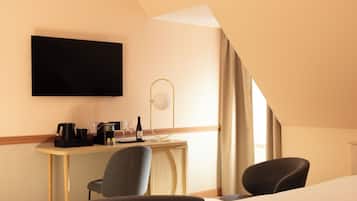 A hotel room with a desk, two chairs, a flat-screen TV, a lamp, and a bed.