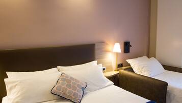 A hotel room with two beds, a nightstand with a lamp, and a wall-mounted light fixture.