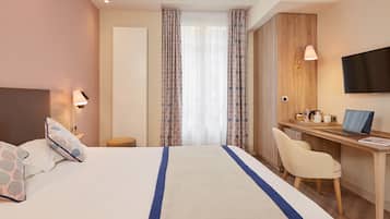Habitación de hotel con cama, escritorio, silla, televisor y ventana con cortinas.