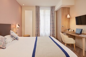 Habitación de hotel con cama, escritorio, silla, televisor y ventana con cortinas.