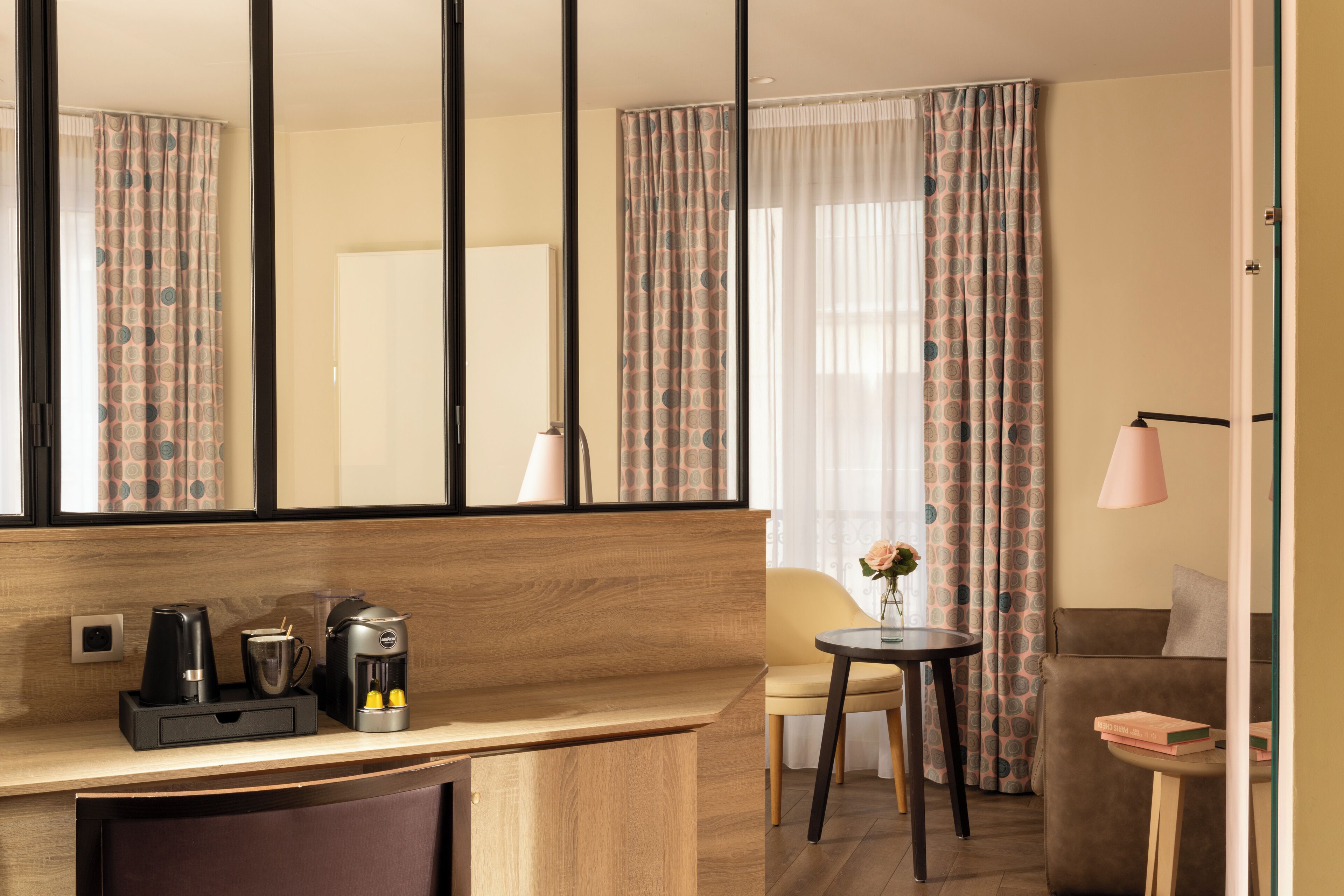 Habitación de hotel con un escritorio de madera, cafetera, una silla, una mesita con un florero y un sofá.
