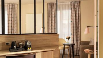 Habitación de hotel con un escritorio de madera, cafetera, una silla, una mesita con un florero y un sofá.