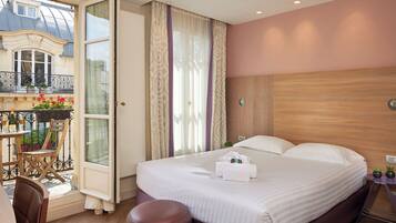 A hotel room with a large bed, a wooden headboard, a small bedside table, and a view of a balcony with flowers.