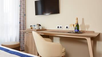 A hotel room with a bed, a desk with a chair, a television, a bottle of champagne, and glasses.