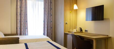 A hotel room with two beds, a desk with a chair, a flat-screen TV, and a window with curtains.
