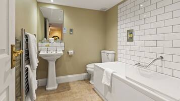 A bathroom with a white sink, toilet, and bathtub, beige walls, and white tiled flooring.