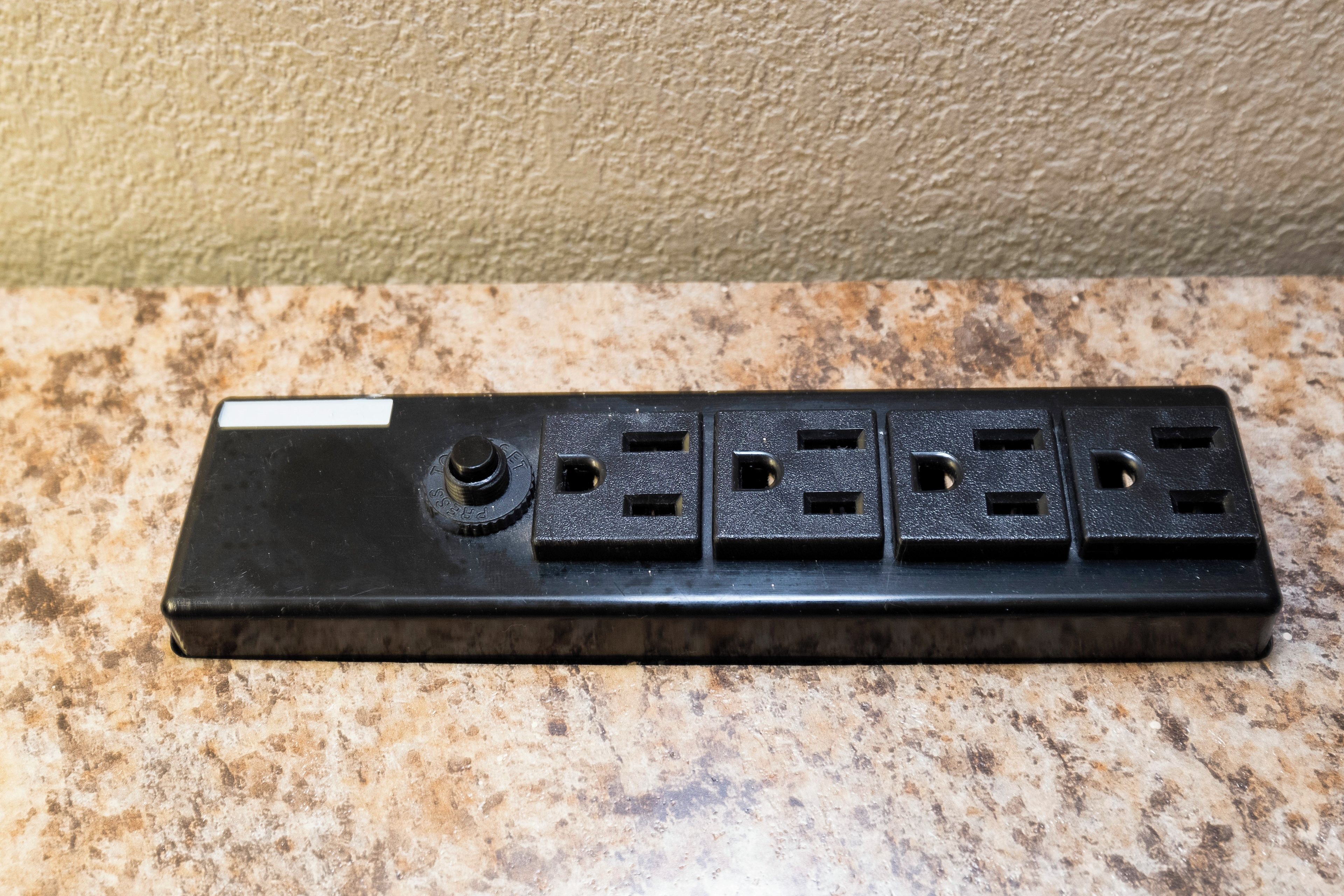 A black power strip with multiple outlets and a switch on a granite countertop.