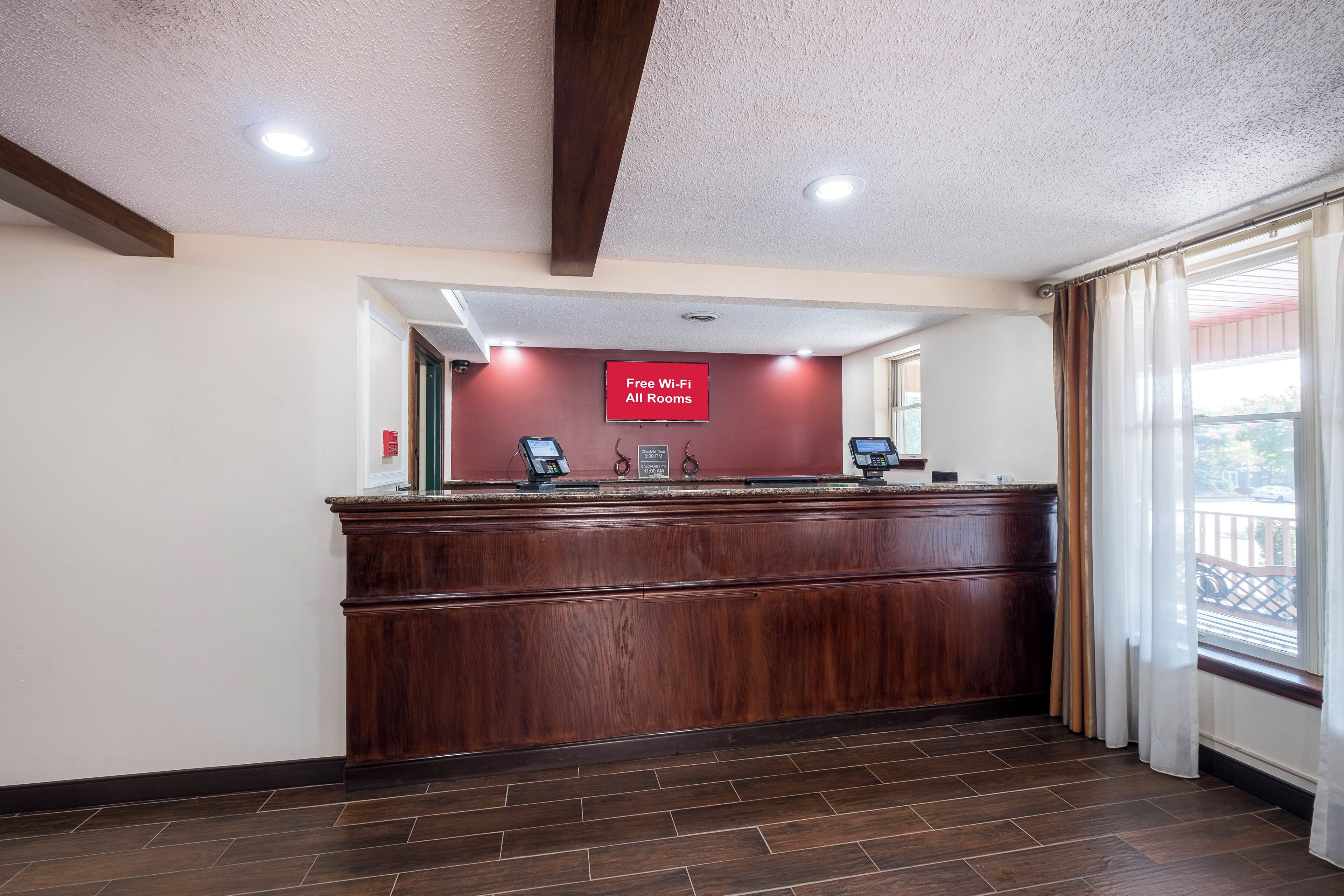 A reception desk with a 'Free Wi-Fi All Rooms' sign, a check-in kiosk, and a view of the outside through a window.
