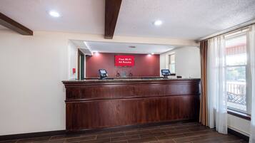A reception desk with a 'Free Wi-Fi All Rooms' sign, a check-in kiosk, and a view of the outside through a window.