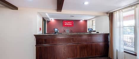 A reception desk with a 'Free Wi-Fi All Rooms' sign, a check-in kiosk, and a view of the outside through a window.