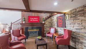 Un hall de hotel con chimenea, sillones de cuero rojo, un televisor de pantalla plana mostrando 'Wi-Fi gratis en todas las habitaciones' y una pared de piedra.