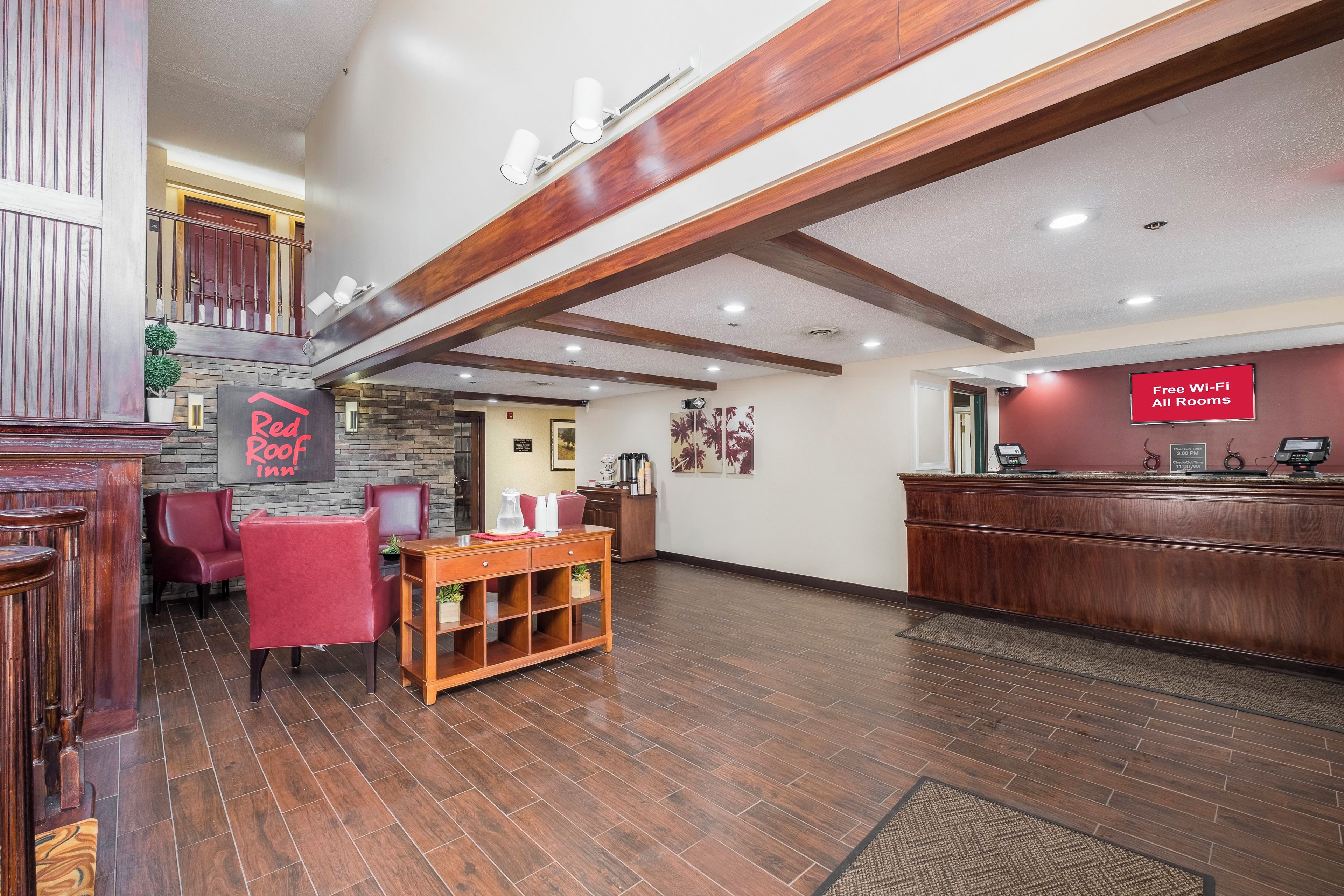 A hotel lobby with a reception desk, a seating area with chairs, a coffee station, and a sign indicating free Wi-Fi availability.