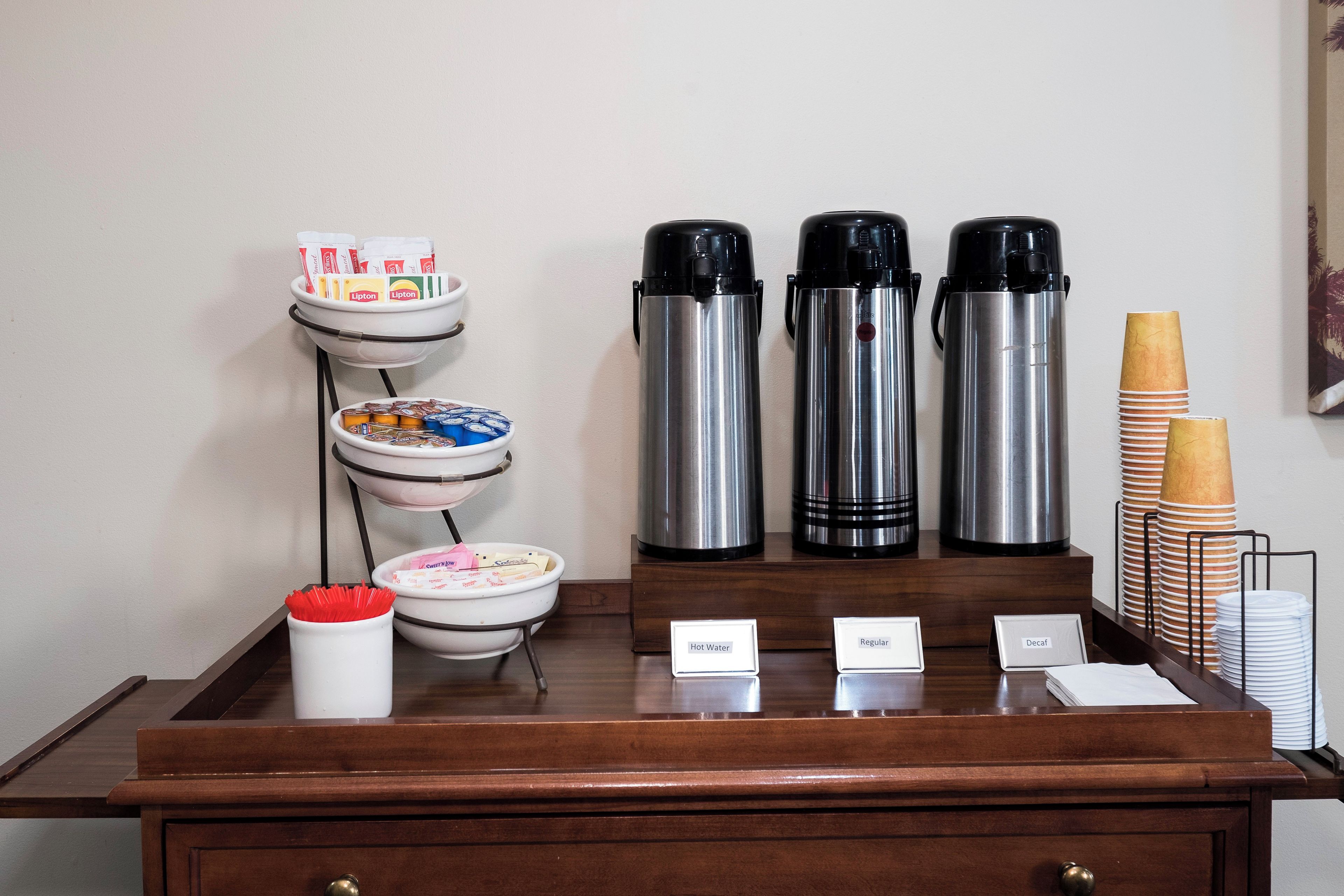 Morgenmadsområde på et hotel med kaffemaskine, teproppen og en skål med cornflakes.