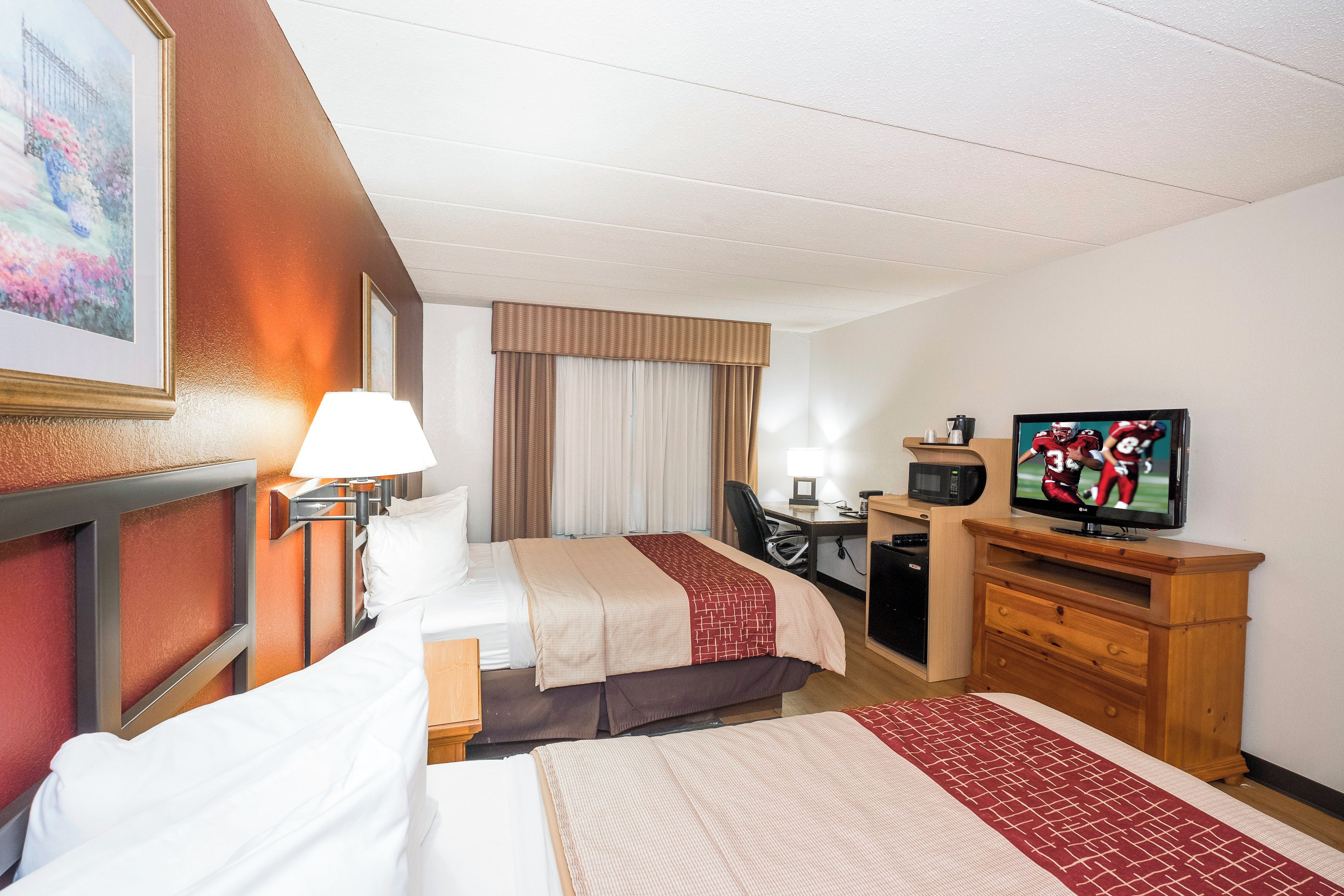 A hotel room with two beds, a desk, a television, and a painting on the wall.