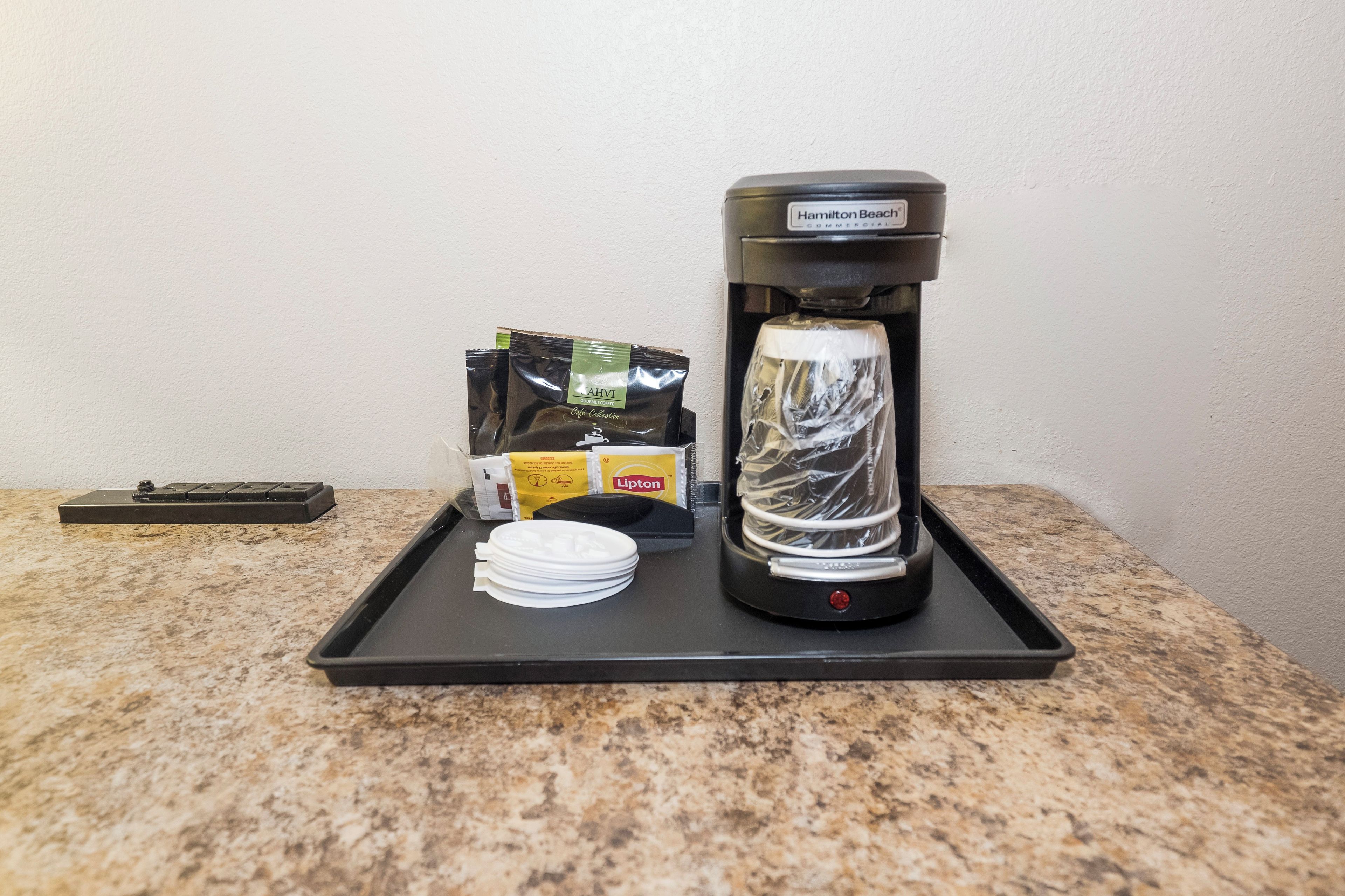 A coffee machine on a tray with coffee pods and a plate of white cups.