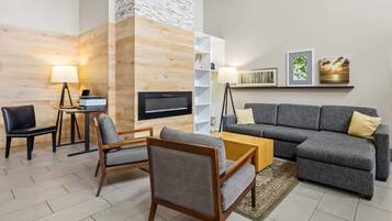 A modern living room with a grey sofa, two armchairs, a coffee table, and a flat-screen TV mounted on a wooden wall.