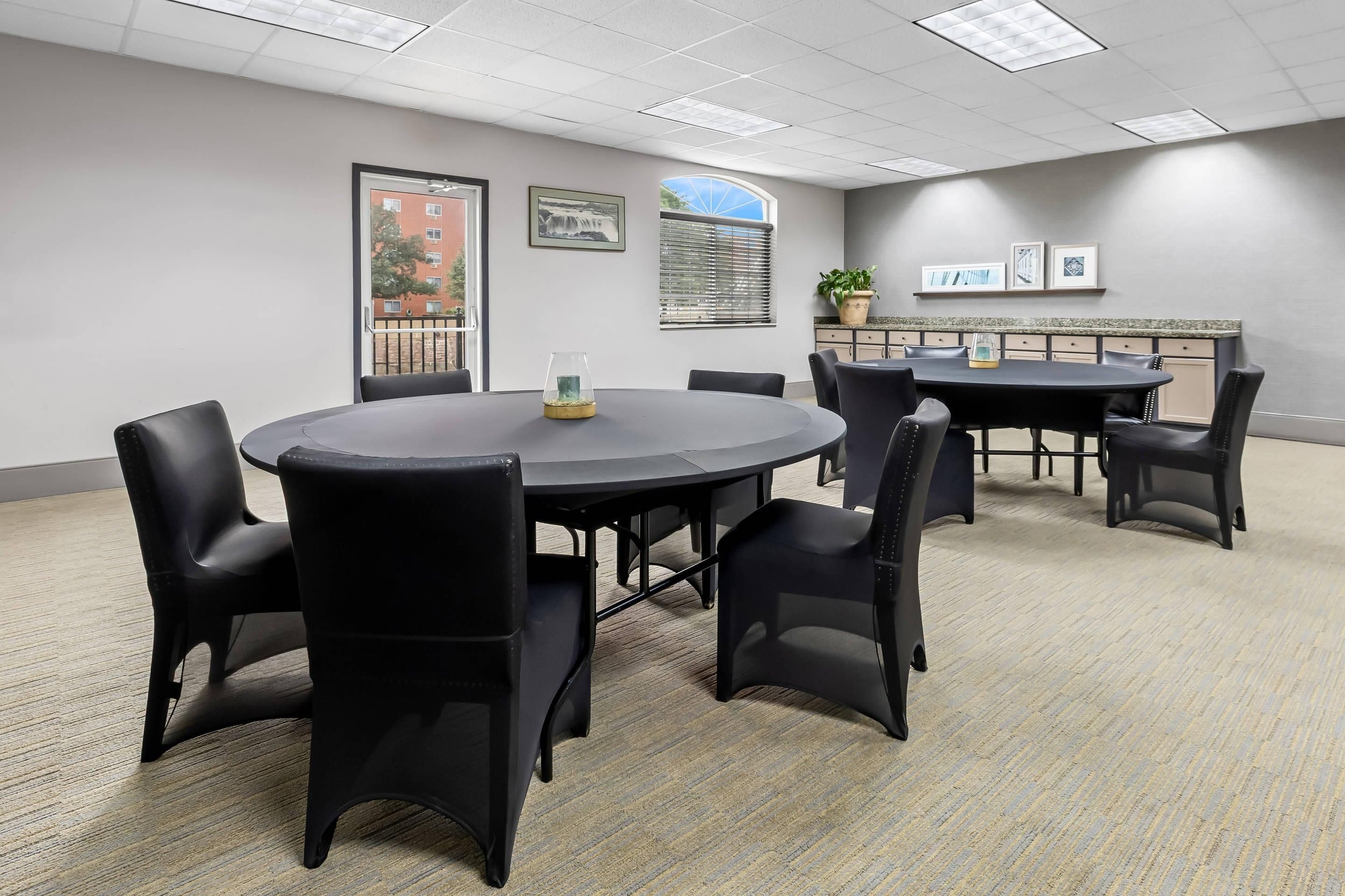 A conference room with a round table and chairs, a potted plant, and framed pictures on the wall.