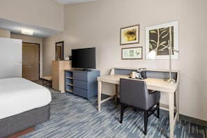 Quarto de hotel com cama, escrivaninha, cadeira, televisão, guarda-roupa e obra de arte na parede.