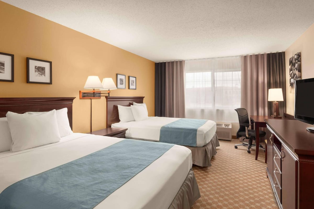 A hotel room with two beds, a desk with a TV, a chair, a desk lamp, and a window with curtains.