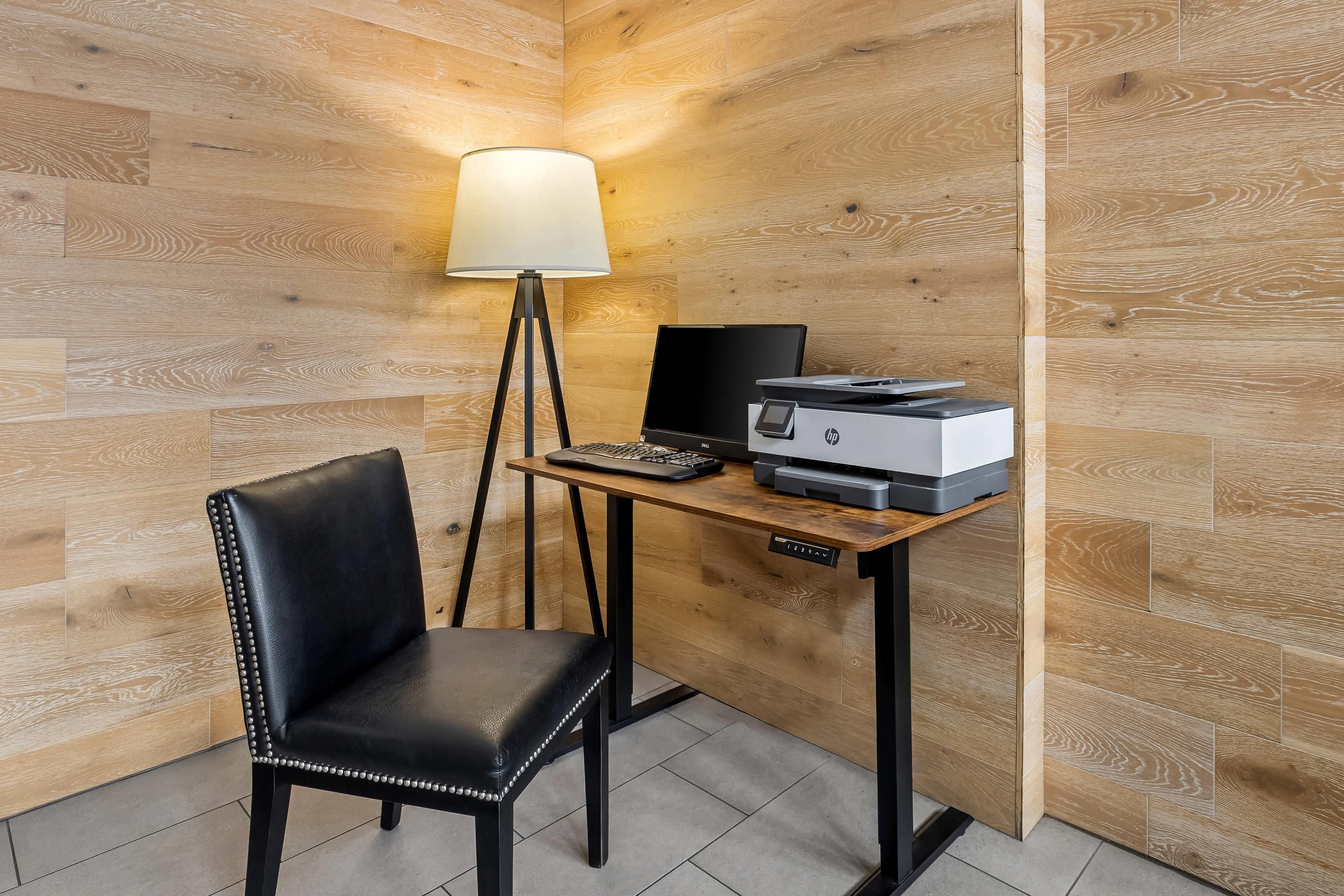 A corner office with a desk, chair, lamp, and printer.