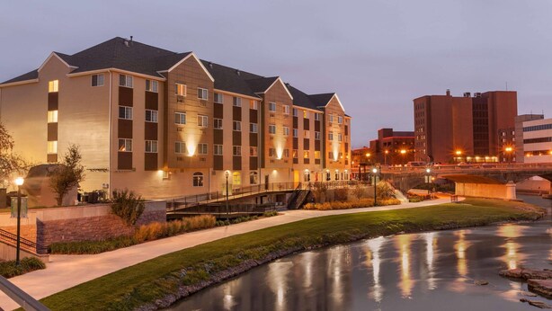 A multi-story hotel with a flat roof, a landscaped area with a water feature, and a bridge connecting to another building. - Country Inn & Suites by Radisson, Sioux Falls (Sioux Falls)
