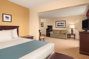 A hotel room with a bed, a sofa, a television, a desk, and a lamp.