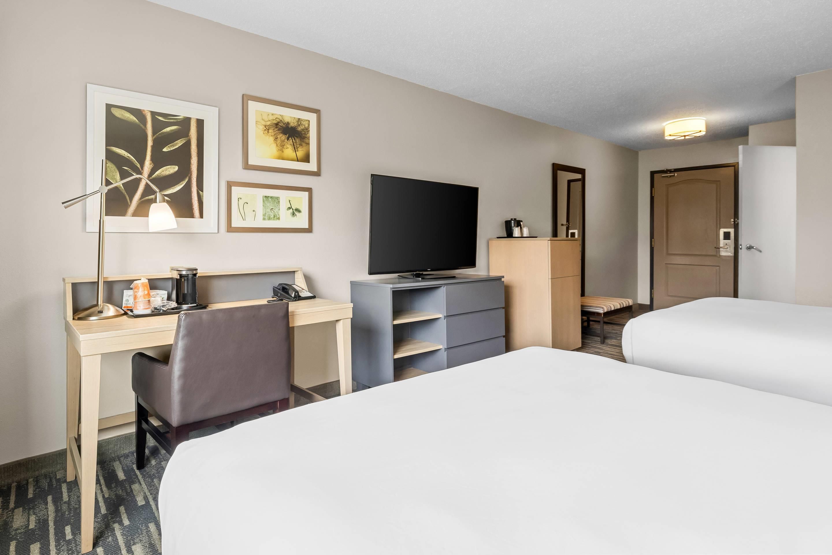 Una habitación de hotel con cama, escritorio, silla, televisor y un cuadro en la pared.