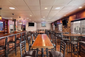 A restaurant with a long wooden table, multiple chairs, a bar area, and a stone wall. - Country Inn & Suites by Radisson, Sioux Falls (Sioux Falls)